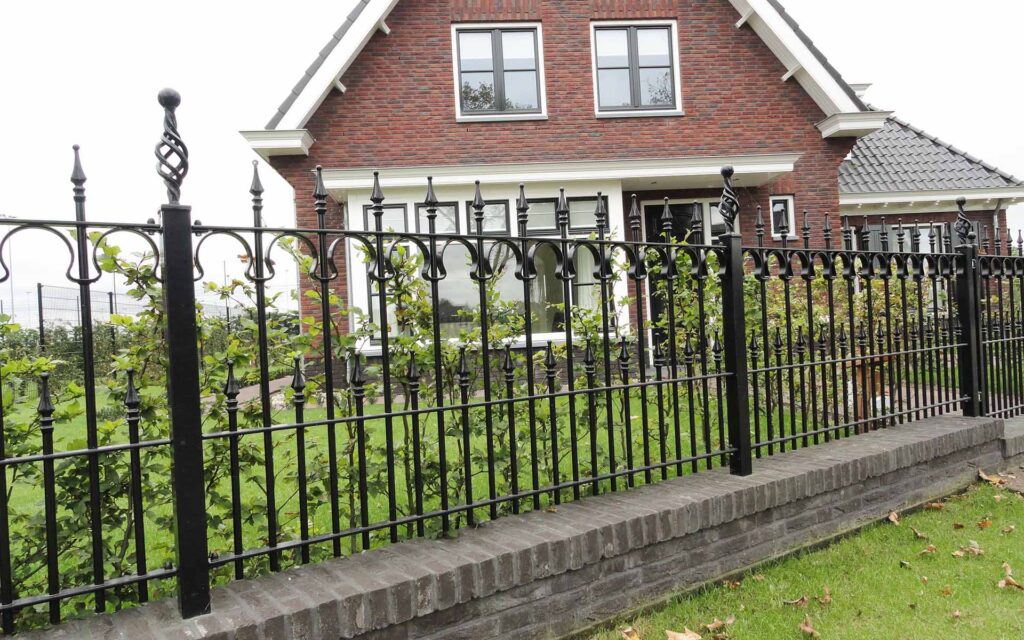 Impressie van een erfgoed met een vrijstaand huis. Het erfgoed is omheind met een zwart sierhekwerk van staal.