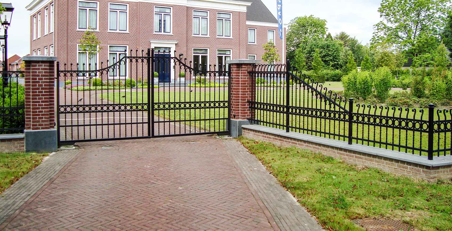 Vanaf een oprit kijken we naar een landgoed met een villa. Het landgoed heeft een riante tuin, met een klassiek hekwerk en klassieke sierpoort als omheining.